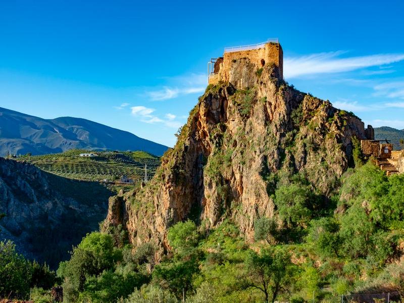 Castle ruins crowning a rocky crag above green terraces in the Alpujarra Granadina — explore Granada's mountains with Andaluciatours.