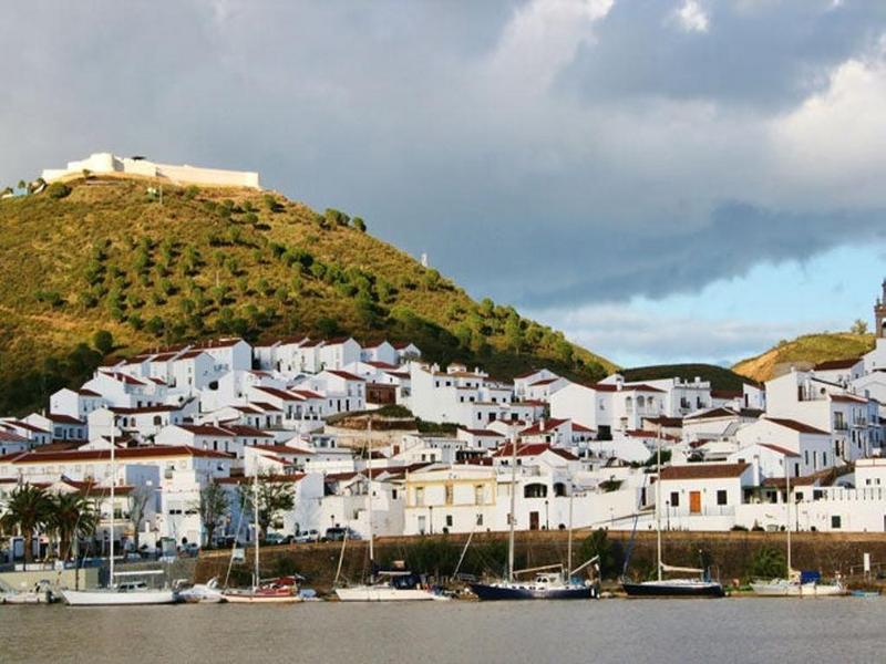 A whitewashed village crowned by a hilltop chapel above the river in El Andévalo, Huelva — visit with Andaluciatours.