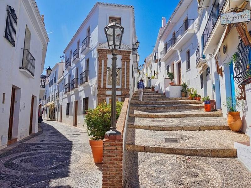 A steep, flower-lined whitewashed street with mosaic paving in an Axarquía village, Málaga — wander with Andaluciatours.
