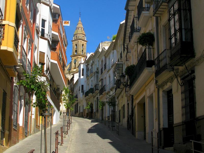 A narrow whitewashed street leading to a Baroque bell tower in the Campiña Sur Cordobesa, Córdoba — wander with Andaluciatours.