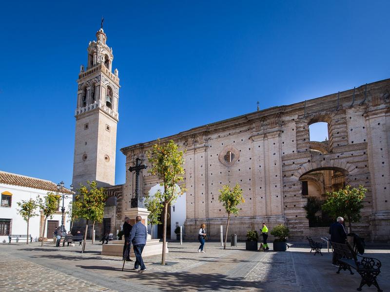 A richly decorated bell tower rising over a sunny plaza in Écija, Seville's city of towers — visit with Andaluciatours.