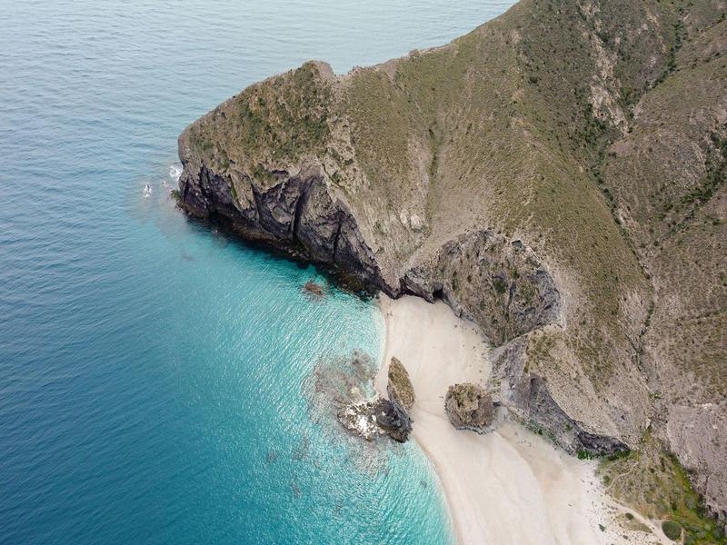 A secluded sandy cove and turquoise water below rugged cliffs in the Levante Almeriense — find hidden beaches with Andaluciatours.
