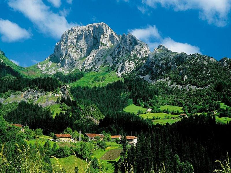 A jagged peak rising above green pastures and scattered farmhouses in Los Montes, Granada — explore with Andaluciatours.
