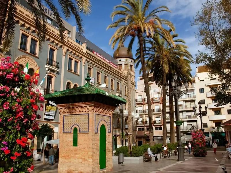 An ornate ceramic monument on a palm-lined plaza in the city of Huelva — explore the Metropolitana de Huelva with Andaluciatours.