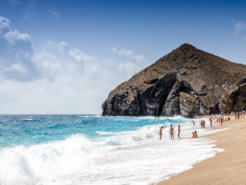 Turquoise waves breaking beside a volcanic rock headland on the Almería coast, Poniente Almeriense — discover it with Andaluciatours.