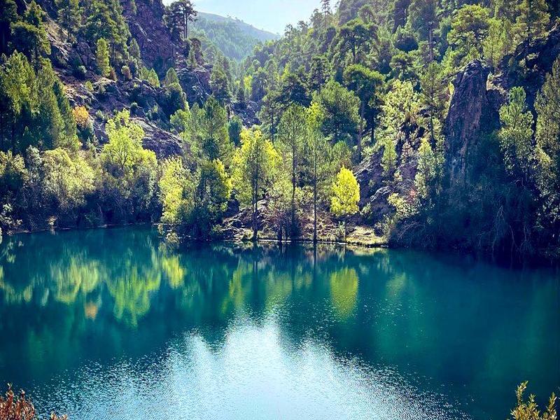 An emerald lake mirroring forested cliffs in the Sierra de Cazorla, Jaén — explore Spain's largest natural park with Andaluciatours.