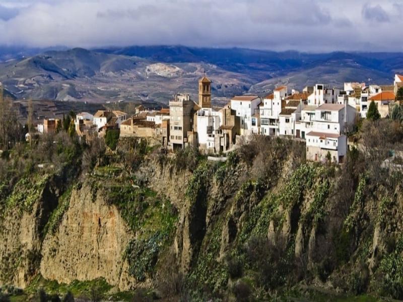A whitewashed village perched on a rocky outcrop with a church tower in the Valle de Lecrín, Granada — visit with Andaluciatours.