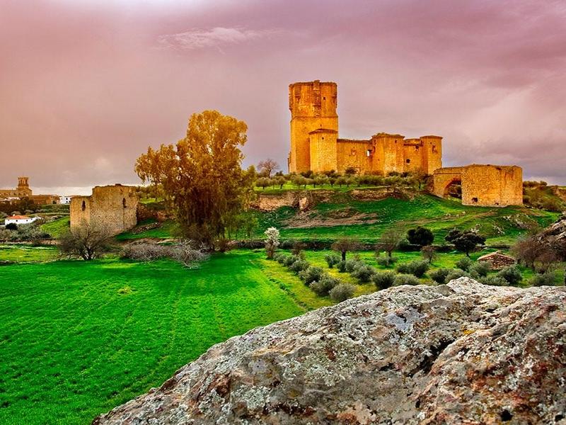 A ruined castle glowing at sunset over green pastures in the Valle de los Pedroches, Córdoba — explore with Andaluciatours.